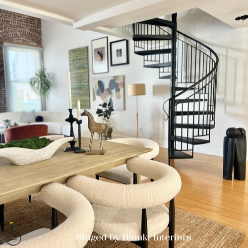 Luxury vacant home staging featuring an open-concept dining area with sculptural seating, warm wood tones, and a statement spiral staircase that highlights architectural character and flow. Staged by Bionki Interiors in Southern California. Luxury vacant home staging featuring an open-concept dining area with sculptural seating, warm wood tones, and a statement spiral staircase that highlights architectural character and flow. Staged by Bionki Interiors in Southern California.